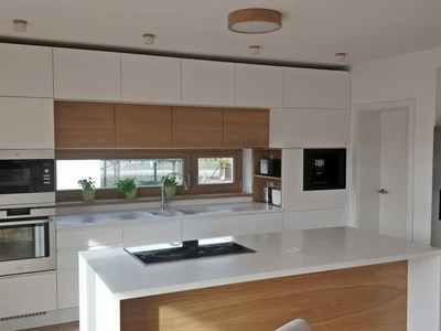 Lakovaná bílá kuchyňská linka v kombinaci s dubovými dýhovanými dvířky, corianovou pracovní deskou a varnou deskou Bora PURE