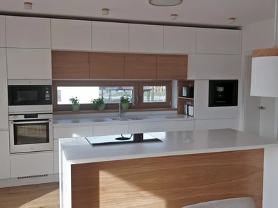 Lakovaná bílá kuchyňská linka v kombinaci s dubovými dýhovanými dvířky, corianovou pracovní deskou a varnou deskou Bora PURE