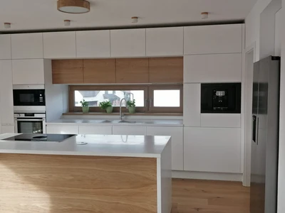 Lakovaná bílá kuchyňská linka v kombinaci s dubovými dýhovanými dvířky, corianovou pracovní deskou a varnou deskou Bora PURE